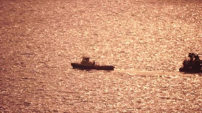 在金色的夕阳下，拖船拉着一艘装满港口起重机的驳船穿过平静的海面。鸟瞰图拖船拖曳大型起重船。水货运输的