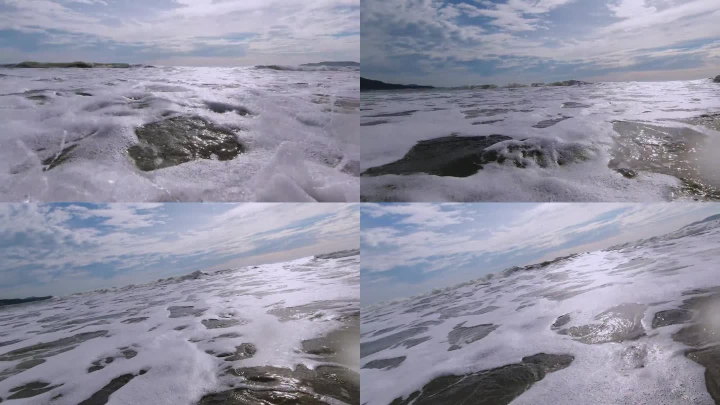 海浪的泡沫浸湿了相机，美丽的阳光明媚的蓝天，背景中有一些云
