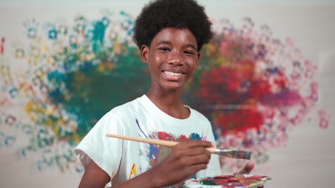 一个非洲男孩站在那里，手里拿着画笔，指着相机。艺术。启迪