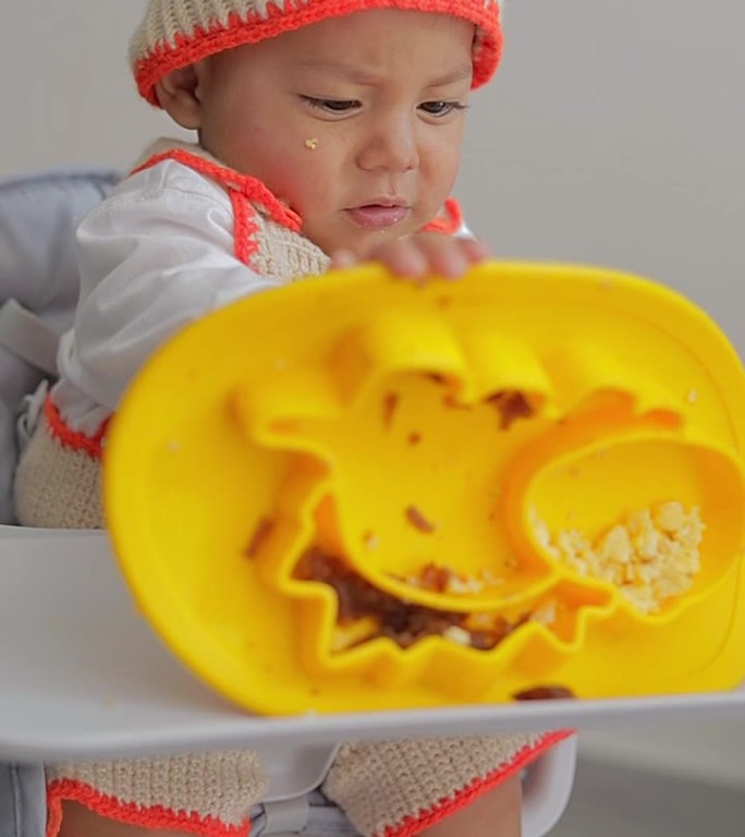 拉丁裔婴儿在家里吃早餐时坐在椅子上玩他的盘子里的食物。婴儿主导的断奶概念