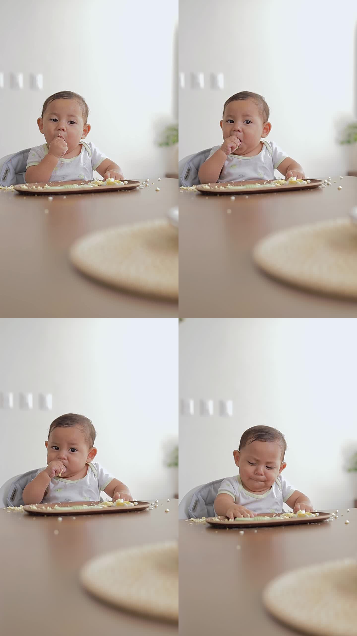 宝宝用手吃着鸡蛋，坐在家里的桌子旁