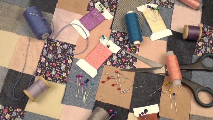 拼布缝纫的配件放在拼布纺织品上，上面有蓝色色调的印花棉布和牛仔布元素