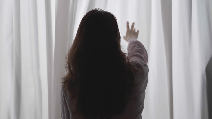 女人站在窗前用手抚摸窗帘背影
