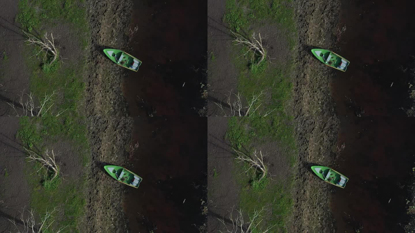 鸟瞰图:无人机发现一艘渔船安全降落在岸边，被蓝色和绿色的宁静色调所拥抱，点缀着倒下的树林。