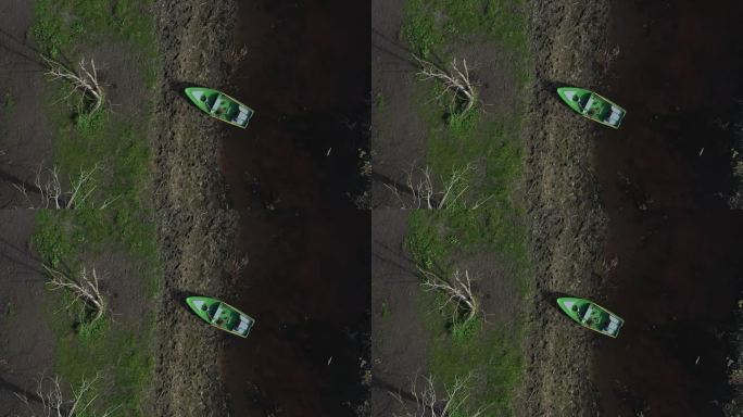 鸟瞰图:无人机发现一艘渔船安全降落在岸边，被蓝色和绿色的宁静色调所拥抱，点缀着倒下的树林。
