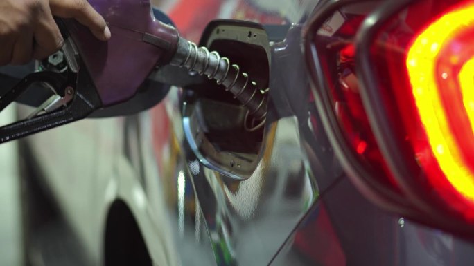 在加油站，一只手将黑色的油嘴伸进汽车的油箱。
