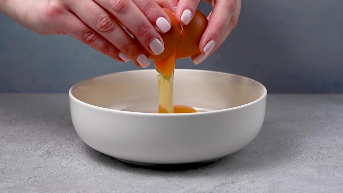 女人的手拿着一个有裂缝的鸡蛋，然后把它打碎。做煎蛋卷，早餐或烘焙。蛋白质食物