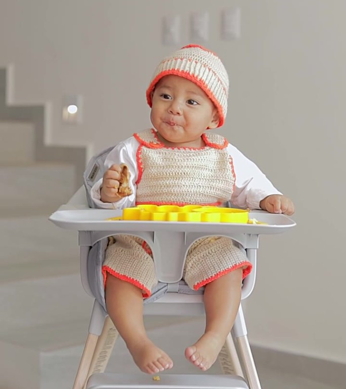 宝宝坐在椅子上用手吃东西，看着镜头微笑着