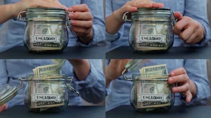面目全非的女人把装满美国货币美元现金钞票的玻璃罐转过来，上面写着“紧急情况”。准备省钱。适度消费和节