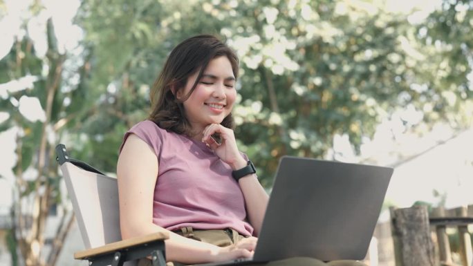 年轻的亚洲女人在咖啡馆用笔记本电脑打字。随时随地工作的概念