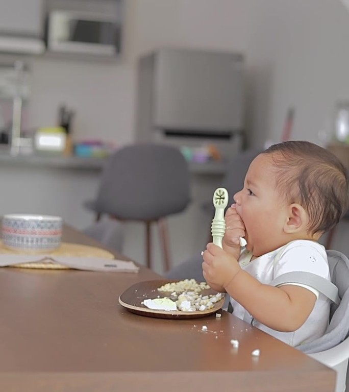 婴儿坐在桌子旁，用手拿着勺子吃东西。