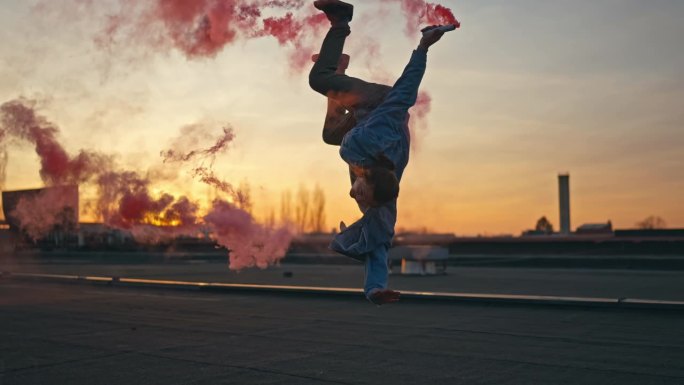 日落时分，青年男子手持烟雾弹在屋顶表演后空翻和霹雳舞