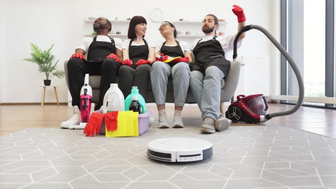 一群管家坐在沙发上，机器人吸尘器在打扫地板。