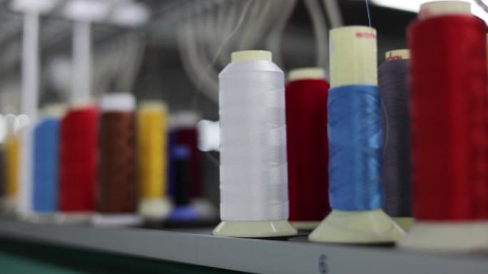 工业纺纱机彩色缝纫线轴和白色丝线的近照。多色筒子在服装生产行业的面料制造厂使用。