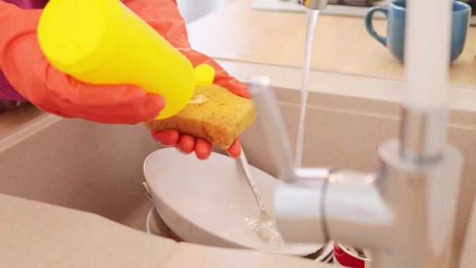 不知名的女人戴着橙色橡胶手套洗碗的人从事日常家务，用水和肥皂确保清洁