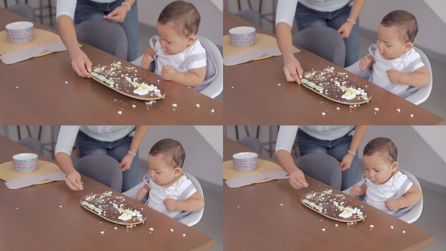 宝宝第一次尝试固体食物，坐在桌子旁吃，妈妈帮他吃。婴儿主导的断奶概念