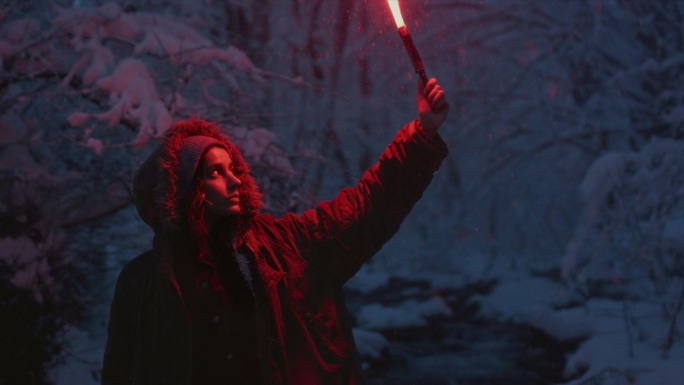 一个小女孩拿着燃烧的信号火。一个女人在冬天的森林里点燃了一个红色的救援信号弹