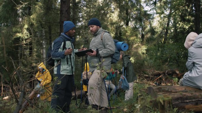 不同的旅行者在森林里用平板电脑讨论小路
