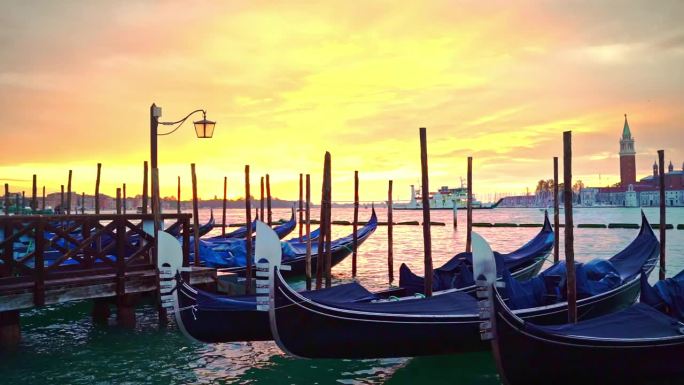 在威尼斯柔和的粉黄色日出中，一艘渡轮穿过摇曳的贡多拉穿过泻湖，一盏灯笼矗立在泻湖蔚蓝的水中