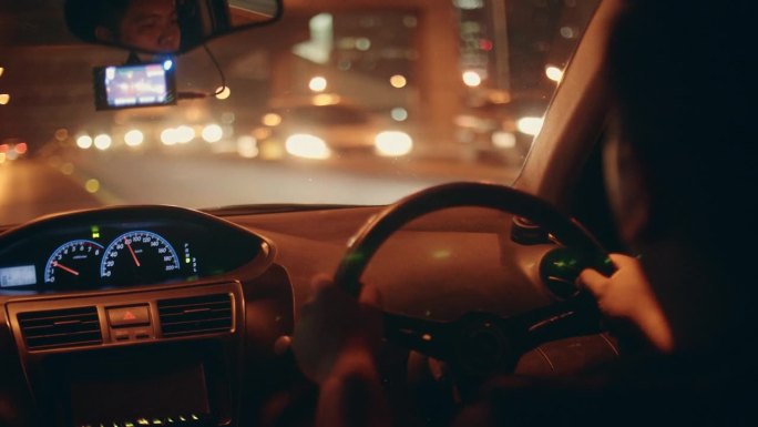夜行之旅:亚洲男人独自思考生活，驱车穿过繁忙的城市景观，驶入夜晚的照明混乱。