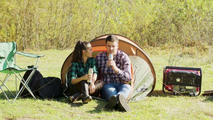 男友坐在他们的露营帐篷前亲吻女友的脸颊