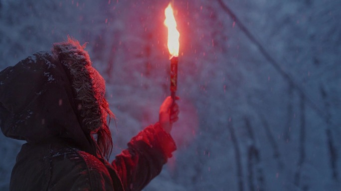 年轻女孩拿着燃烧的信号火。一个女人在冬天的森林里点燃了红色的救援信号弹