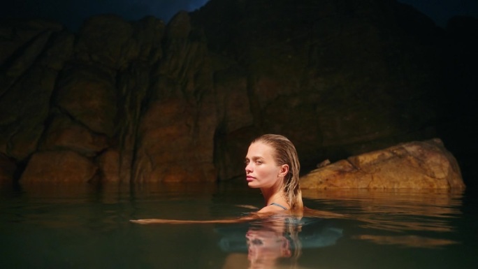 神秘的蓝色女子在夜晚游泳，宁静的美丽在自然池，周围的岩石，反射月光。空灵恬静的场景，滋润肌肤，唤起宁