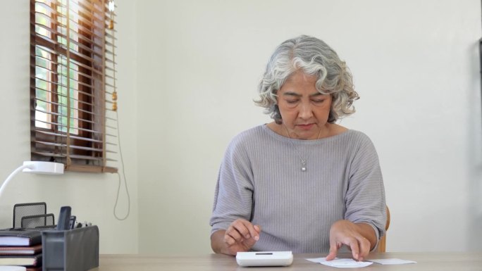 年长的女性在网上计算、写作、支付账单，在家工作时准备财务报告。专注于成熟女性，从事会计工作，忙于财务