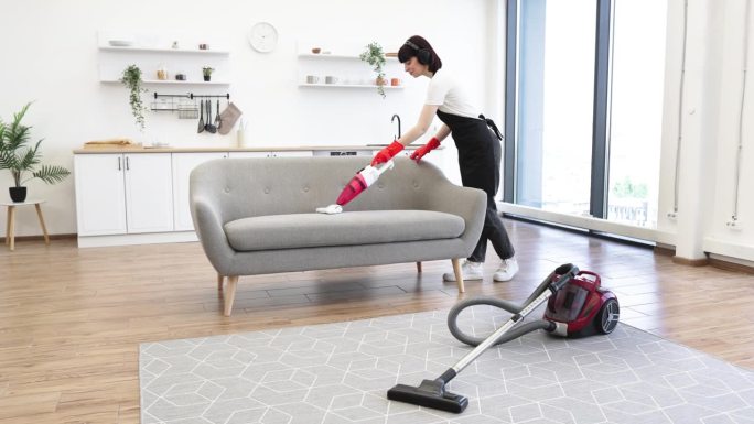专业年轻清洁工用手提无绳吸尘器为沙发吸尘。