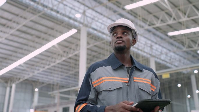 黑人男性品管经理观察纸制品生产车间近景，检查工厂生产机械和产品质量。