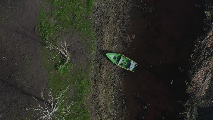 从上面拍摄:无人机暴露了一艘停在海岸线上的渔船，在散落的倒下的树林中创造了蓝色和绿色的鲜明对比。