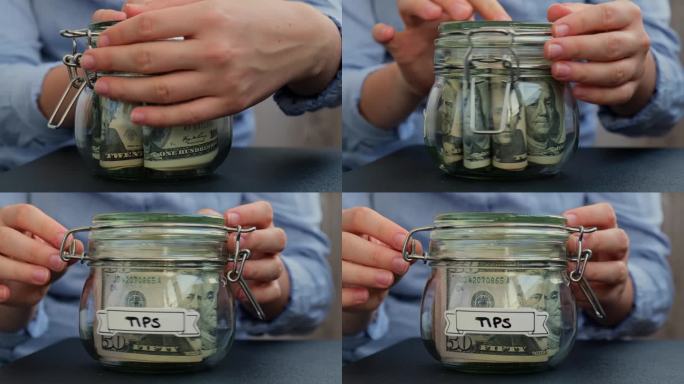 女人的手在存钱，把装满美元钞票的玻璃罐打开。TIPS转录在罐子前面。管理个人财务，为未来的不安全感增