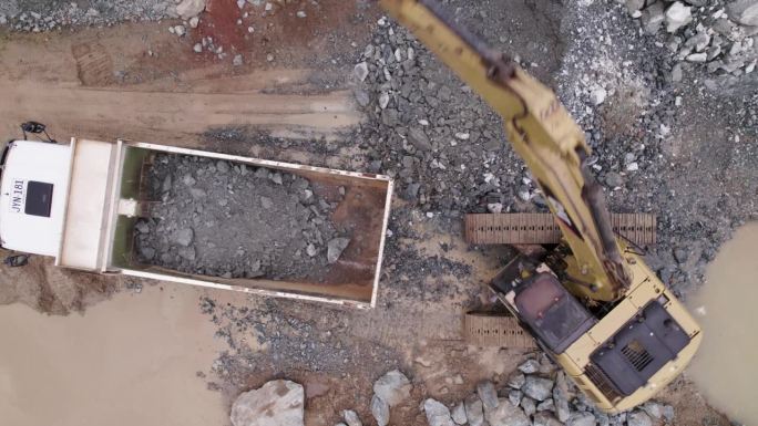 一架动态无人机拍摄的一台挖掘机将其产出倒入采矿卡车。