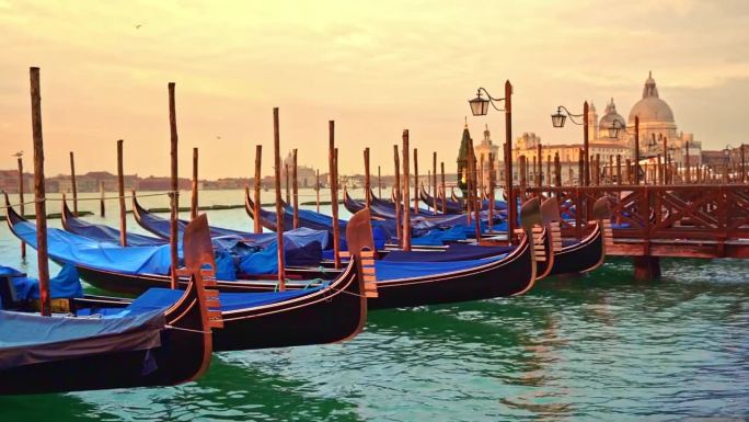 在威尼斯柔和的黄色日出中，摇曳的贡多拉、灯笼矗立在蔚蓝的泻湖上，还有圣玛丽亚致敬大教堂，把天空染成了