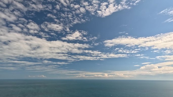 在平静的海面上，蓝色的夏日天空中飘动着飘忽的蓬松积云。抽象的空中自然夏季海洋日落，大海和天空的看法。