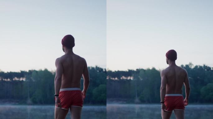穿着游泳短裤的帅哥穿过草地走向湖边，看着湖水