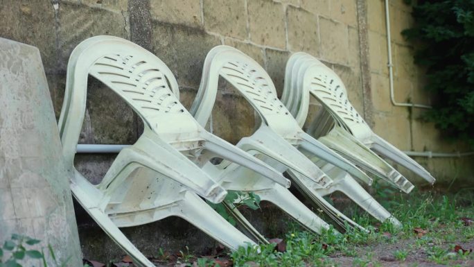 旧的塑料椅靠在室外的墙上，废弃的塑料家具放在杂乱的地方准备处理和回收，以解决环境污染问题