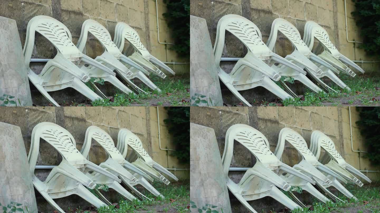 旧的塑料椅靠在室外的墙上，废弃的塑料家具放在杂乱的地方准备处理和回收，以解决环境污染问题