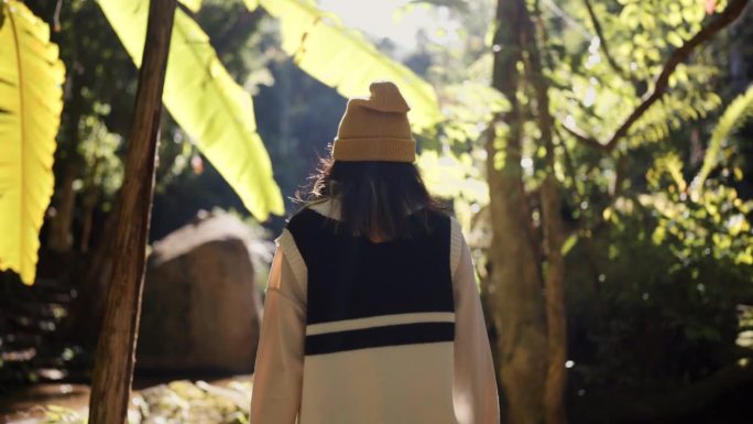 亚洲妇女穿着暖和的衣服走在森林里，感到精神焕发，心情愉快