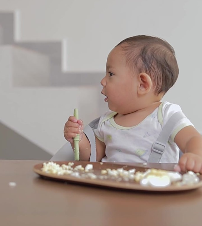 拉丁裔婴儿坐在桌子旁吃饭时嚼着勺子