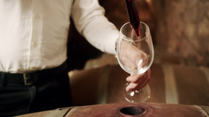 男酿酒师在酒厂用移液管将桶装红酒倒入玻璃杯中
