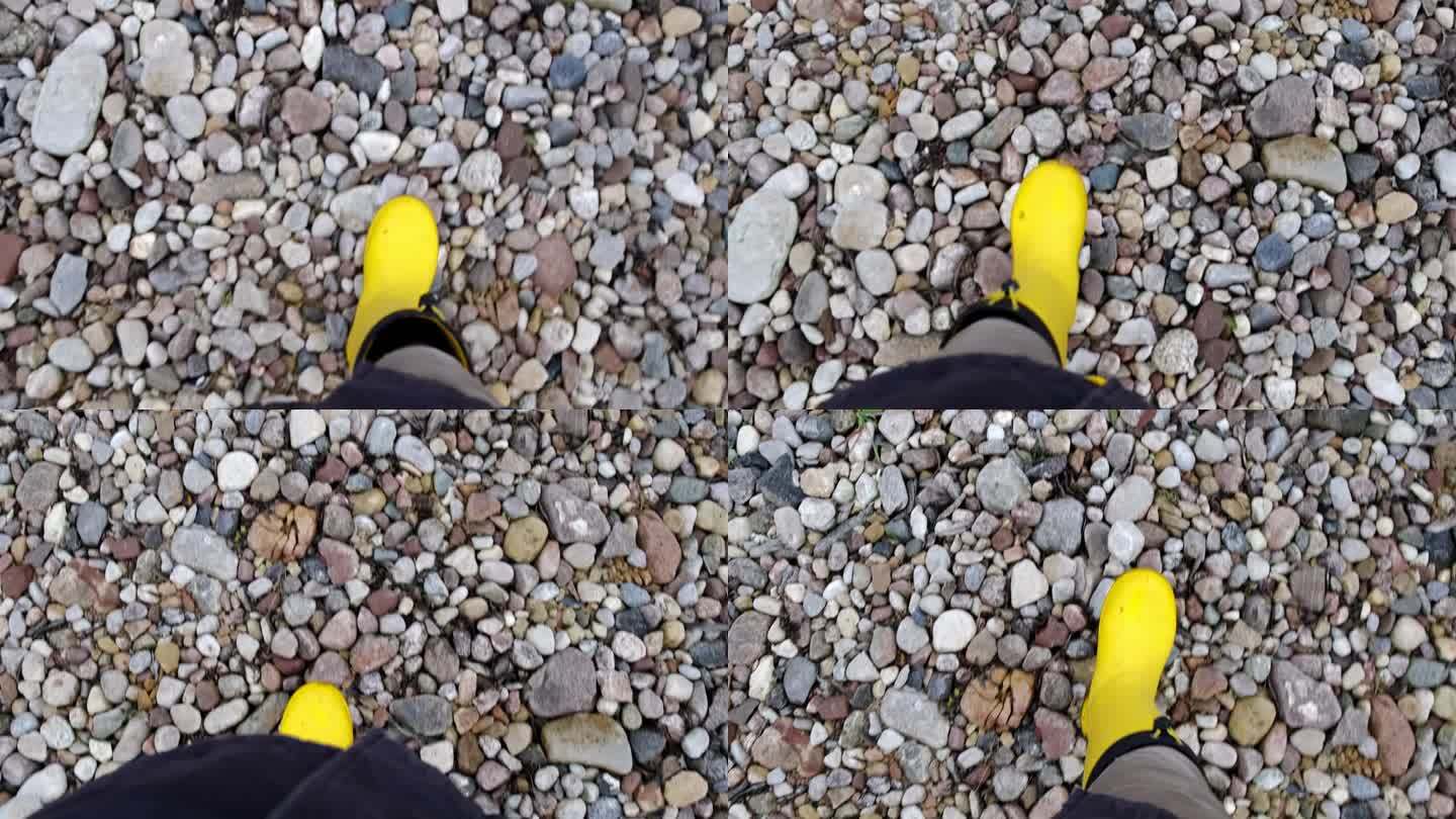 园丁脚踩黄色胶靴，走在碎石地上、道路上。石头表面。秋天的季节。特写镜头。从上面看。身体的部分。农夫在