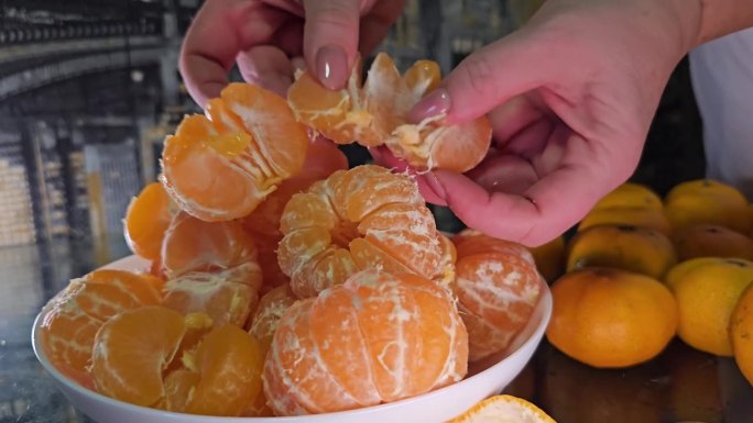将去皮的橘子放在白色盘子里，切成片。女性的手准备柑桔汁。