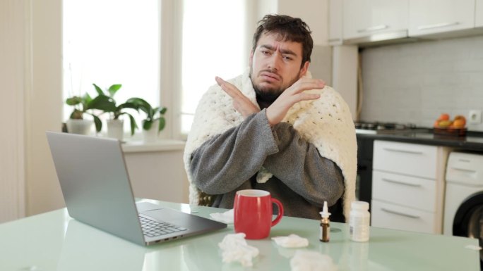 患流感的男子在家里用毯子裹着笔记本电脑，发出“x”信号