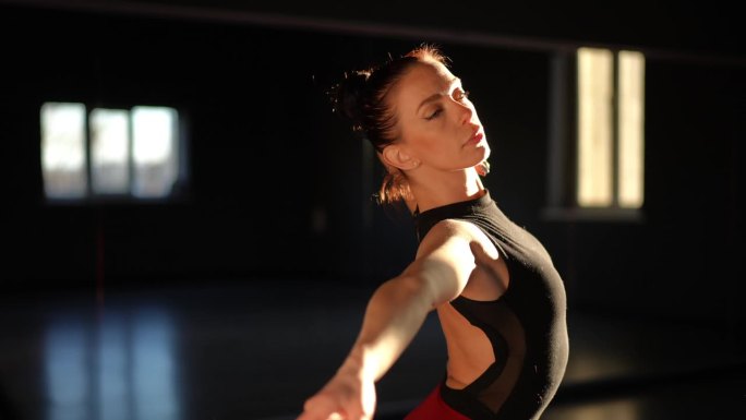 一位美丽的芭蕾舞女演员站在舞蹈大厅里，用她的手臂和身体做着流畅的动作。