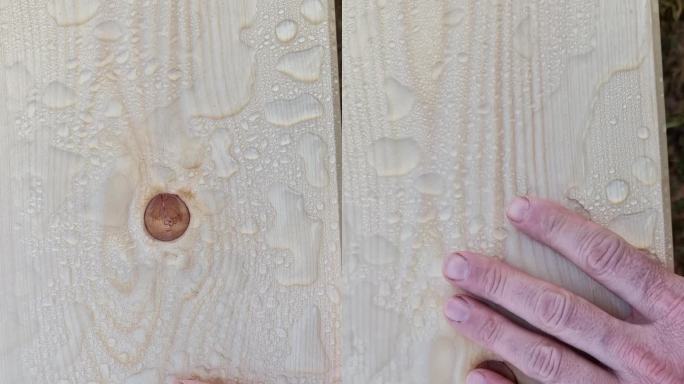 一个人在擦漆板上的水。他对板子的浸渍效果很好感到满意。水滴聚集在一起，不会渗入木材