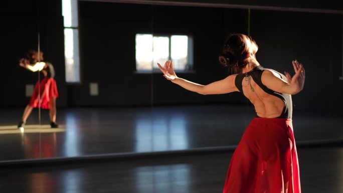 一位芭蕾舞演员站在舞蹈大厅的镜子前，用手做着动作。