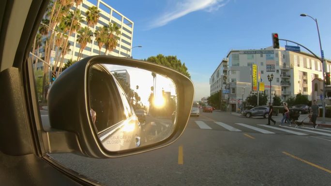 驾驶POV洛杉矶市中心与日落在后视镜看到。在棕榈树下的林荫大道上开车