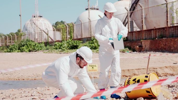 穿着化学防护服的团队生态学家从炼油厂从下水道收集石油中的有毒物质，以防止化学污染和生物危害。