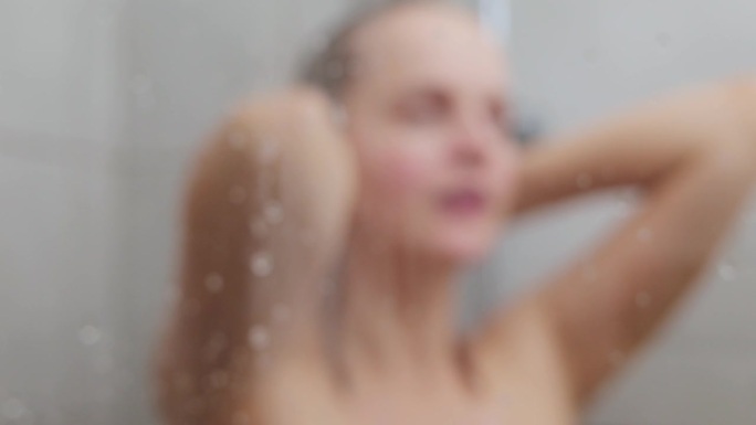 家庭spa。美容习惯。放松的淋浴。日常护肤品。年轻的成年女子在蒸汽模糊的玻璃后面用水滴洗头发和身体